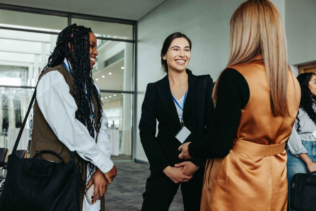 Three women wearing conference badges chatting and laughing about regional differences in the Lingala language