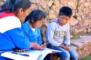 a woman teaching two children while sitting on the stones outside
